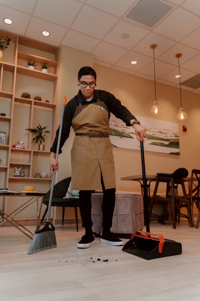 A man in an apron sweeping the floor of a cozy and stylish indoor room.