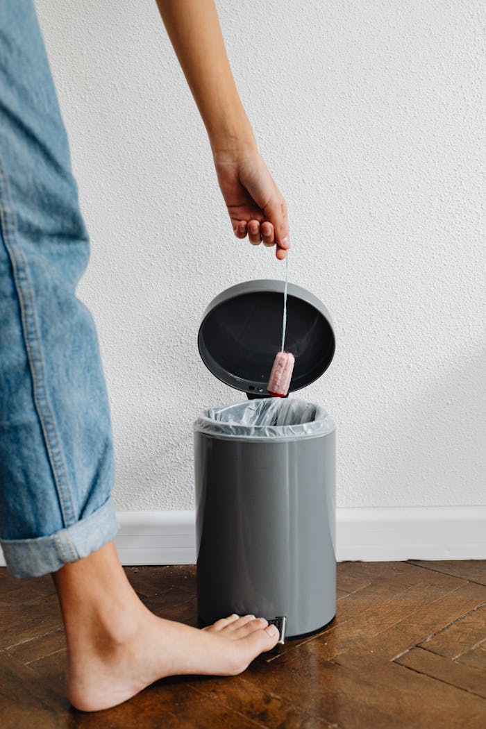 Close-up of a person throwing a used tea bag into a gray kitchen trash bin.